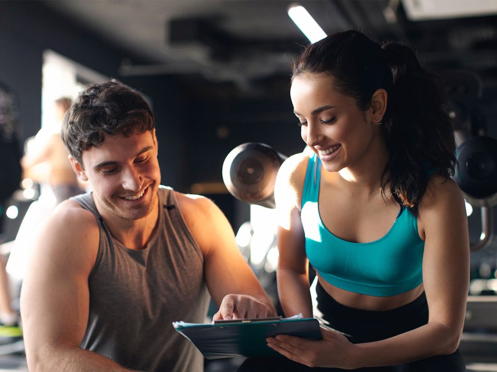 Man in gym giving female instructor feedback on iPad